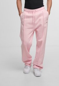 Pink sweatpants with a relaxed fit, elastic waistband, and side seam details, paired with white sneakers. Smooth fabric texture is visible.