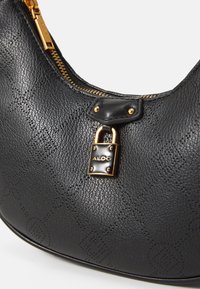 Sort læderhåndtaske med en struktureret overflade, guldfarvede detaljer og en lås. Designet er buet med lynlås-lukning.