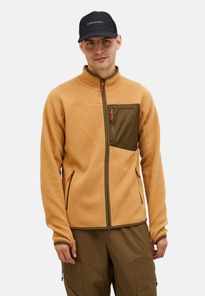 Fleece jacket in light brown with a dark green chest pocket. Features zippered pockets and contrasting orange zipper pulls. Smooth texture.