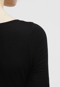 Camisa de algodón negra, diseño ajustado, de manga larga, textura suave, con un escote redondeado que destaca la zona de la espalda y los hombros.