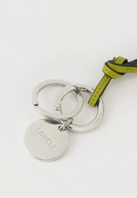 Võtmehoidja, mis koosneb kahest omavahel ühendatud hõbedasest rõngast ja ümmargusest hõbedasest sildist, millel on reljeefne kiri "LANCEL". Omab rohelist nahast detaili.