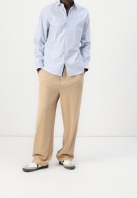 Ljust blå randig skjorta med knappar, beige byxor och grå skor med vita och svarta accenter. Tyget ser slätt ut; skorna har en sportig design.