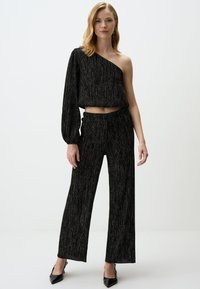 Zwart tweedelig outfit met een een-schouder cropped top met lange mouw en wijde broekspijpen, van textuurstof met metallic draden.