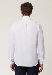 Chemise blanche à manches longues avec un col classique, une texture lisse, des poignets à bouton, un ourlet arrondi et une fente discrète au dos.