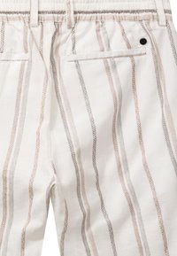 Pantalon blanc à rayures verticales beige et grises, taille élastique, passants pour ceinture, et poches passepoilées à l'arrière, dont une avec un bouton noir.