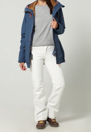 Chaqueta exterior azul con capucha forrada en marrón, sudadera gris debajo, pantalones blancos y botas marrones con cordones amarillos. Texturas lisas y diseño funcional.