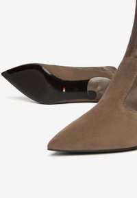 Stivali ankle in suede marrone con punta appuntita e suola in gomma nera, caratterizzati da un tacco leggero e dettagli testurizzati sulla suola.