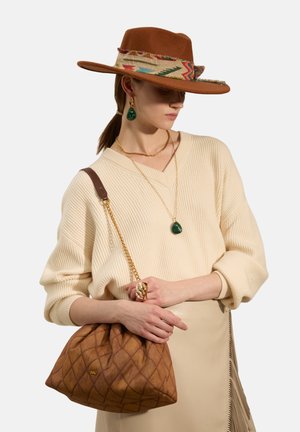 Brown quilted handbag with a gold chain strap, worn with a cream ribbed sweater. Features a wide-brimmed hat with a colorful patterned band.