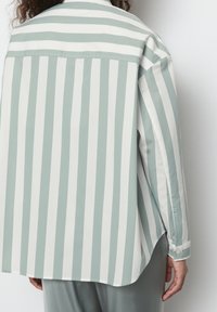 Camisa a rayas verde claro y blanca, abotonada con cuello, con un corte relajado y mangas largas. Tejido suave con un leve brillo.