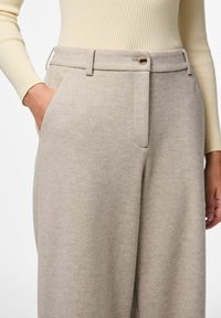 Lichtbeige op maat gemaakte broek van textuurstof, met een rechte pijp, zijzakken, een knoopsluiting en een subtiel visgraatpatroon.