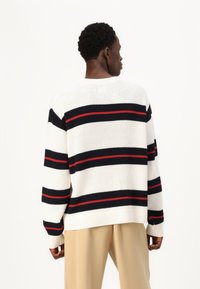 Suéter de punto blanco con rayas horizontales en azul marino, rojo y negro. Presenta una textura acanalada, un ajuste holgado y un escote redondo.