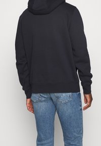 Sudadera azul marino con un bolsillo tipo canguro, puños y cinturilla acanalados; combinada con unos vaqueros de color azul claro que cuentan con dos bolsillos traseros.