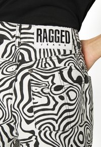 Pantalones vaqueros de patrón en blanco y negro con diseños en espiral, con una etiqueta "RAGGED JEANS" en la cinturilla y un detalle en el bolsillo trasero.