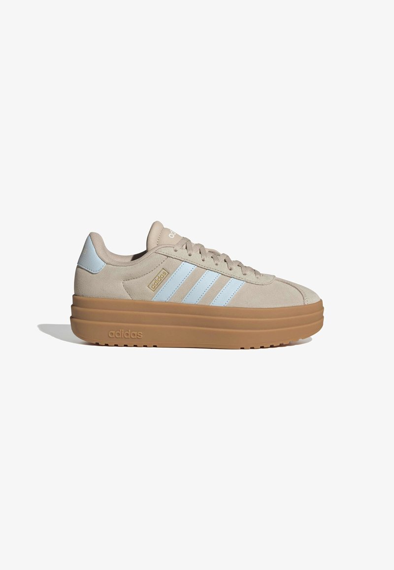 Beige suede Adidas sneaker with white stripes and logo, thick light brown sole, and lace-up closure, viewed from the outer side.