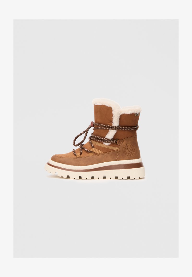Botas de tobillo de ante marrón con forro de piel de fur, suela gruesa beige y cordones marrones. Presenta un parche con el logo en el lateral.