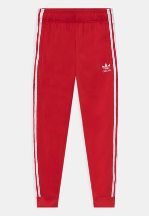 Pantalones deportivos rojos de Adidas con rayas blancas laterales, cintura elástica, tobillos puñados y logo de Adidas en el muslo superior izquierdo.