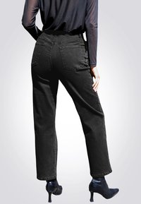 Pantaloni neri in denim a vita alta con taglio dritto, dotati di tasche posteriori e finitura testurizzata, abbinati a scarpe nere con tacco alto.