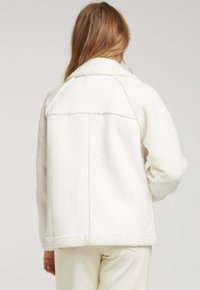 Veste en polaire blanche avec un panneau arrière lisse contrastant, dotée d'un col et de manches texturées. Design simple sans embellissements.