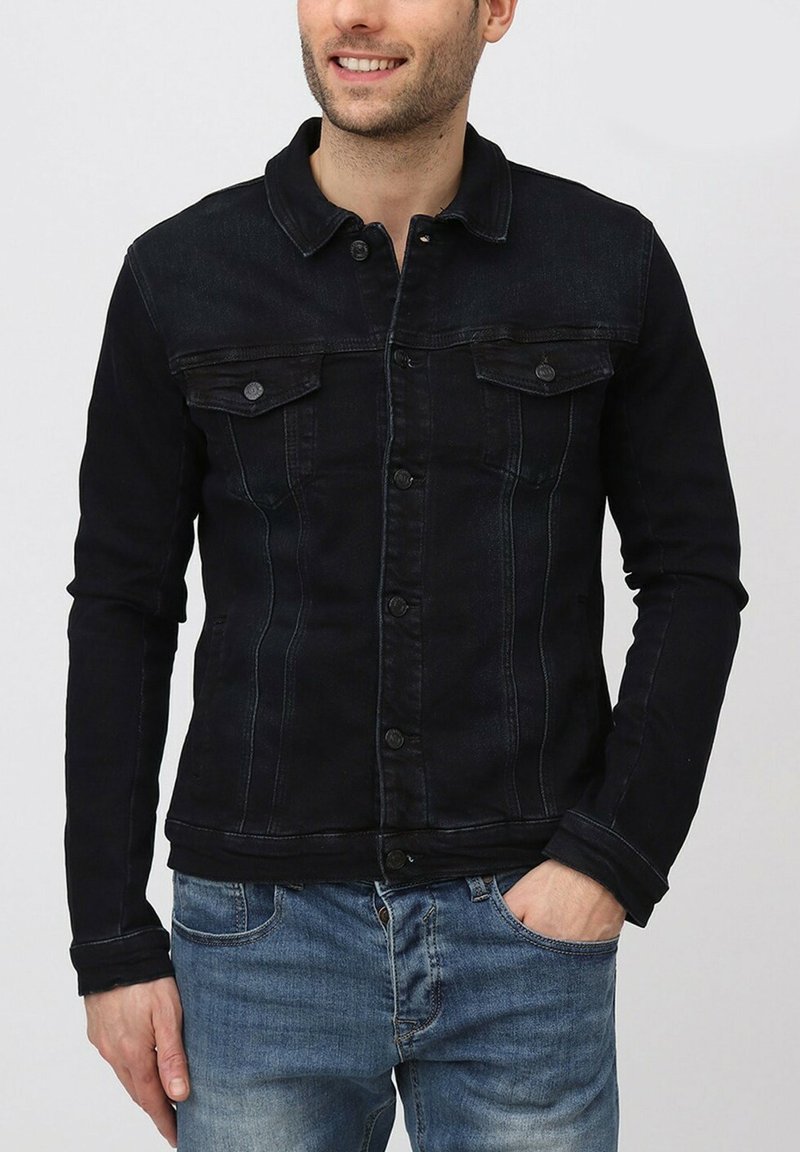 Veste en denim noir avec fermetures à boutons, deux poches poitrine et coutures contrastées. Présente un col classique et une coupe ajustée.