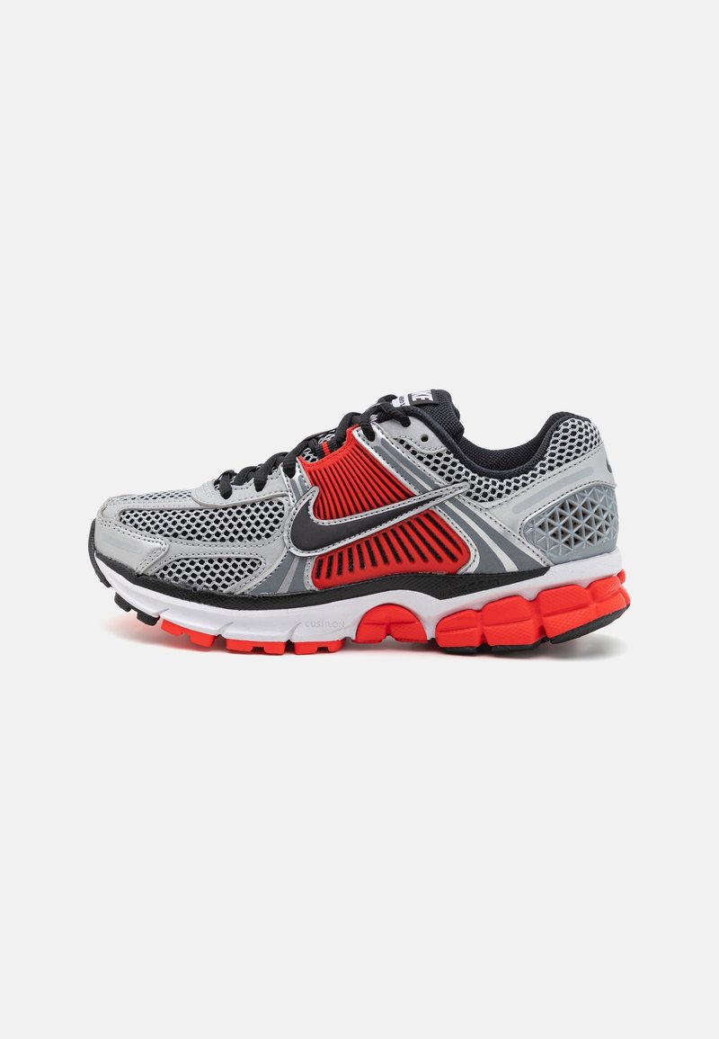 Gray and red athletic shoe with mesh upper, black accents, padded collar, and textured sole. Features cushioned midsole and prominent branding.