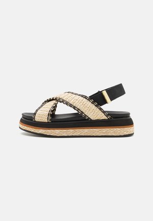 Sort platformsandal med naturlige vævede krydsede stropper og flette-detalje på sålen, der har en sort hælrem med guldlås.