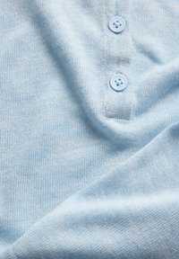 Tissu tricoté bleu clair doux avec deux boutons assortis sur une patte, montrant une texture détaillée et de légers plis.