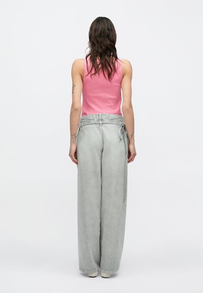 Ροζ αμάνικη μπλούζα συνδυασμένη με φαρδιά, ανοιχτό γκρι τζιν παντελόνια με λεπτομέρεια δεσίματος στη μέση και απαλή υφή.