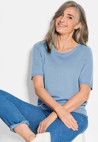Hellblaues T-Shirt mit kurzen Ärmeln und Rundhalsausschnitt, geripptem Muster, kombiniert mit hochgekrempelten Jeans und weißen Sneakers.