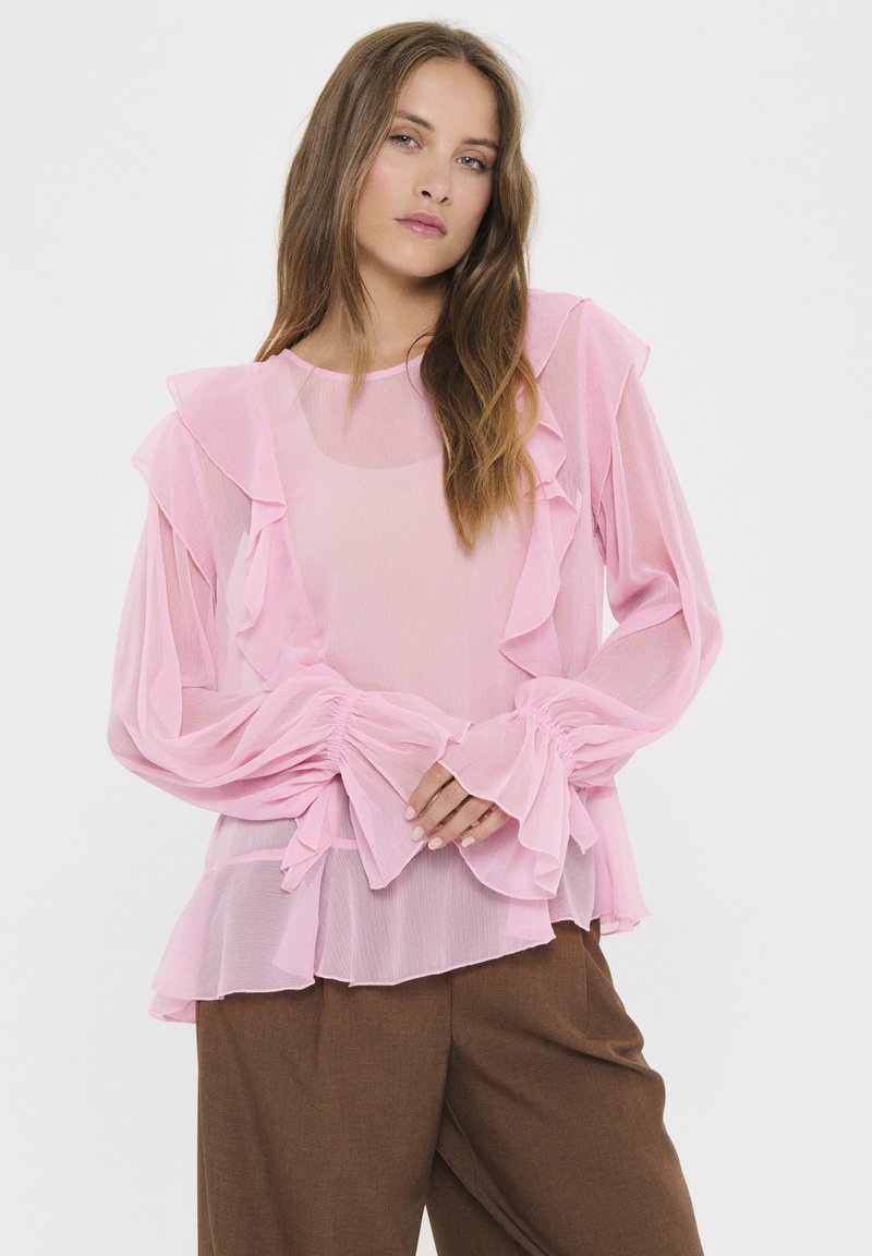 Rosa, durchsichtige Bluse mit Rüschendetails an den Ärmeln und dem Körper, elastischen Bündchen und einem ausgestellten Saum. Zarte Textur im gesamten Stoff.