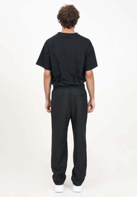 T-shirt nero a maniche corte e pantaloni neri abbinati. I pantaloni presentano una cintura elastica e una tasca posteriore. Il modello indossa sneaker bianche.