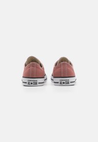 Crvene platnene tenisice s niskim dizajnom, s crnim gumenim potplatima i bijelim trakama. Na stražnjem dijelu prikazana je oznaka "CONVERSE ALL STAR".