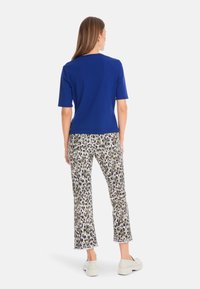 Blue short-sleeve top paired with white pants featuring a green and black leopard print. Lightweight fabric with a relaxed fit and hem.