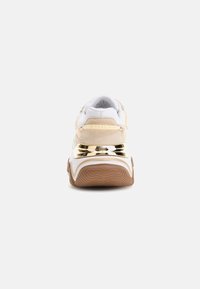 Sneaker realizzati in tessuto bianco con accenti beige, dettagli metallici dorati sul tallone e una suola in gomma testurizzata.