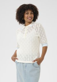 Virkat polo-sweater i krämfärg med en delikat öppen design, korta ärmar, ljusblå krage och ribbade muddar. Avslappnad passform med fickor.