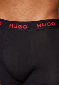Boxeri negri, cu un design ajustat și o textură netedă. Talie elastică cu inscripția "HUGO" în litere roșii.