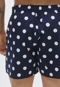 Tengerészkék úszónadrág fehér pöttyös mintával, rugalmas derékpánttal, laza szabással és puha anyagtextúrával.