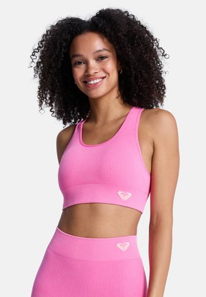 Roze geribbelde sportbeha met brede bandjes en een cropped pasvorm, met een klein hartjeslogo in het midden. Zachte, elastische stof.