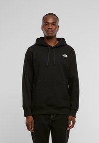 Czarna hoodie z kapturem, wykonana z miękkiego materiału, z przednią kieszenią, ściągaczami przy mankietach oraz małym białym logo na lewej piersi.