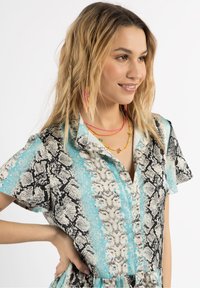 Rochie cu mânecă scurtă, prezentând un imprimeu de piele de șarpe în alb și negru, cu accente turcoaz. Butoni pe partea din față și o croială lejeră.