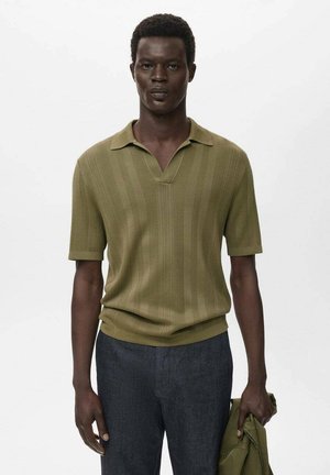 Olive green short-sleeve polo shirt with vertical ribbed texture and a V-neck, paired with dark pants, and a light jacket held in the hand.