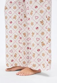 Φωτεινό κρεμ παντελόνι πιτζάμας με επαναλαμβανόμενο μοτίβο από ανθρωπάκια τζίντζερμπρεντ, μπισκότα και καρδιές σε αποχρώσεις καφέ και κόκκινου. Μαλακό ύφασμα και άνετη, ευρεία εφαρμογή.