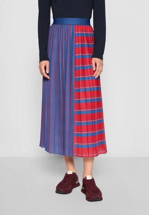 Jupe midi plissée avec un design coloré composé de sections bleues et rouges, agrémentée de rayures. Assortie à des baskets noires.