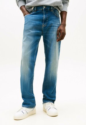 Jeans de mezclilla azul claro con un corte relajado, textura desgastada, cinco bolsillos y cremallera, combinados con zapatillas blancas.