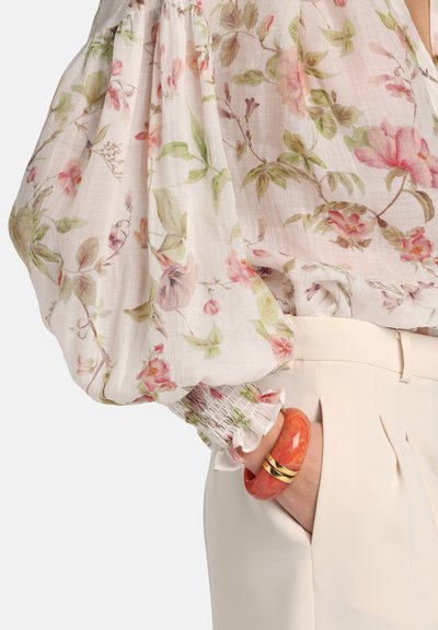 Virágmintás blúz áttetsző, könnyű anyagból, puffos ujjakkal; pasztell rózsaszín és zöld virágok díszítik. Narancssárga márványozott karkötő arany részletekkel.