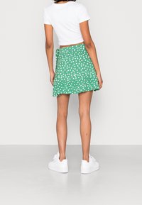 Grøn nederdel med hvide prikker, flæset kant og bindedetalje, parret med en tætsiddende hvid crop top og hvide sneakers.