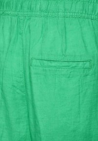 Green fabric pants with an elastic waistband and a single back welt pocket, showing fabric texture and stitching details.