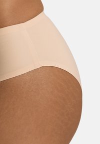 Licht perzikkleurige hooggetailleerde slip met een gladde, rekbare stof en een naadloos ontwerp met een subtiele glans.