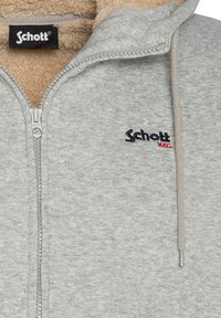 Hoodie gris à fermeture éclair avec une doublure douce en fausse fourrure marron. Comprend un logo sur la poitrine gauche et une fermeture éclair argentée avec une tirette texturée.