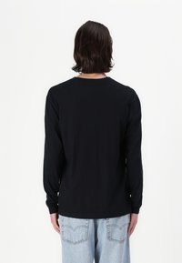 Garās piedurknes melna kokvilnas krekls ar noapaļotu kaklu, ar standarta aprocēm un taisnu apakšmalu. Valkāts ar gaiši ziliem džinsiem.