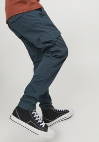 Marinblå cargobyxor med elastiska mudd, sidofickor och en knappdetalj, i kombination med svarta högsta sneakers och vita snören.